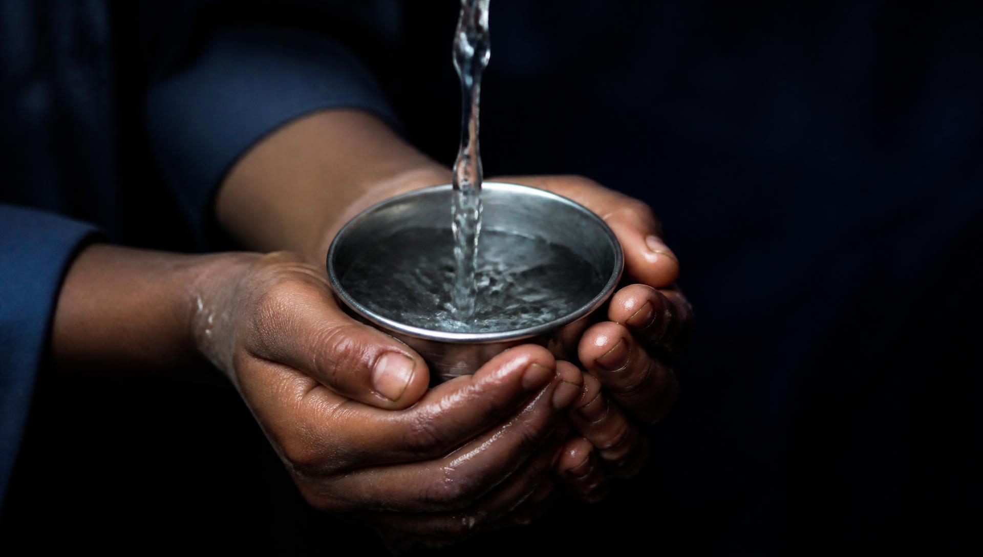 A child's hands holding a plain cup as clear water is poured into it.